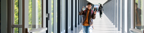 student walking through campus giving the peace sign